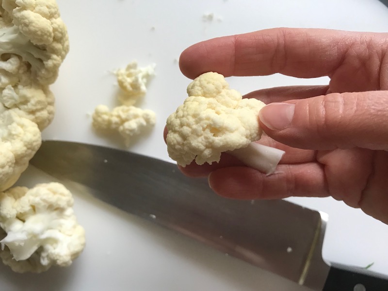 Knife cutting cauliflower for Baked Coconut Cauliflower Bites. They have a slightly sweet and salty crunch outside from the shredded coconut and panko mixture. The inside is soft and creamy. Dip in the Sriracha Mayo. Baked, not fried, so healthy! Easy to make, easy to eat! #cauliflowerrecipes #healthyrecipes #sidedishes #appetizers #healthysnacks