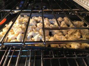 Coconut Cauliflower Bites baking in the oven. They have a slightly sweet and salty crunch outside from the shredded coconut and panko mixture. The inside is soft and creamy. Dip in the Sriracha Mayo. Baked, not fried, so healthy! Easy to make, easy to eat! #cauliflowerrecipes #healthyrecipes #sidedishes #appetizers #healthysnacks