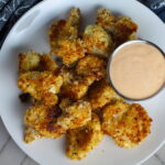 Baked Coconut Crispy Cauliflower Bites on plate with Sriracha Mayo dipping sauce.  They have a slightly sweet and salty crunch outside from the shredded coconut and panko mixture.  The inside is soft and creamy.  Dip in the Sriracha Mayo. 