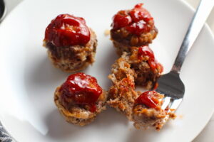 Mini Meatloaf Muffins on a plate. They have only 5 simple ingredients, cook in 30 minutes, and are gluten free. Parmesan gives salty and nutty flavor.  Ketchup on top cooks down into a thick, deep-flavored tangy, salty, and sweet glaze.