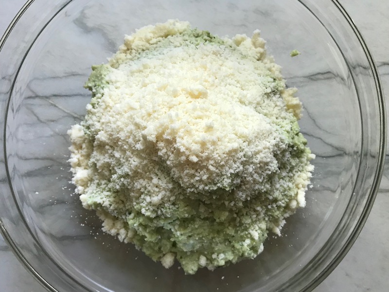 Parmesan Cheese added to pesto in a bowl for Broccoli Pesto Pasta. It's delicious AND good for you! It has all of the classic pesto flavors from garlic, basil, parmesan cheese, and pine nuts. But the flavor is a bit more mellow by adding broccoli! #broccolirecipes #pesto #pasta #easydinner #dinnerideas #familydinner