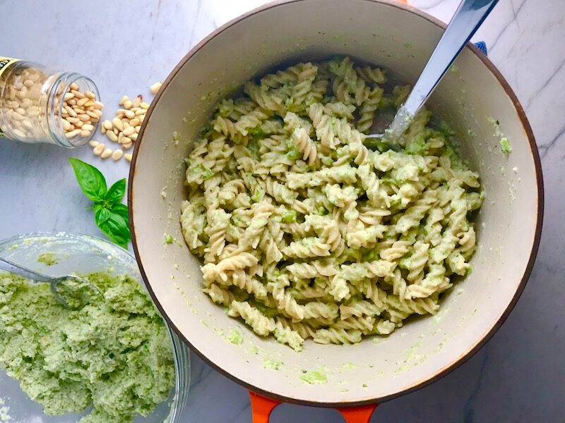 Broccoli Pesto Pasta in pot with spoon with pine nuts and basil on counter. It's delicious AND good for you! It has all of the classic pesto flavors from garlic, basil, parmesan cheese, and pine nuts. But the flavor is a bit more mellow by adding broccoli! #broccolirecipes #pesto #pasta #easydinner #dinnerideas #familydinner