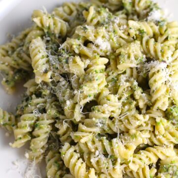 Broccoli Pesto Pasta on a plate with parmesan on top. It's delicious AND good for you!  It has all of the classic pesto flavors from garlic, basil, parmesan cheese, and pine nuts.  But the flavor is a bit more mellow by adding broccoli! #broccolirecipes #pesto #pasta #easydinner #dinnerideas #familydinner