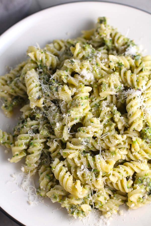 Broccoli Pesto Pasta on a plate with fork and pine nuts and basil on counter. It's delicious AND good for you! It has all of the classic pesto flavors from garlic, basil, parmesan cheese, and pine nuts. But the flavor is a bit more mellow by adding broccoli! #broccolirecipes #pesto #pasta #easydinner #dinnerideas #familydinner