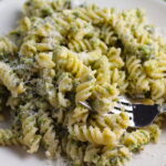 Broccoli Pesto Pasta on a plate with fork in pasta. It's delicious AND good for you!  It has all of the classic pesto flavors from garlic, basil, parmesan cheese, and pine nuts.  But the flavor is a bit more mellow by adding broccoli! #broccolirecipes #pesto #pasta #easydinner #dinnerideas #familydinner