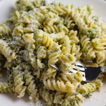Broccoli Pesto Pasta on a plate with fork in pasta. It's delicious AND good for you! It has all of the classic pesto flavors from garlic, basil, parmesan cheese, and pine nuts. But the flavor is a bit more mellow by adding broccoli! #broccolirecipes #pesto #pasta #easydinner #dinnerideas #familydinner
