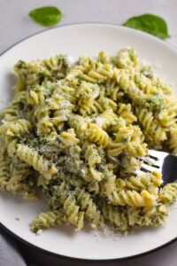 Broccoli Pesto Pasta on a plate with fork in pasta. It's delicious AND good for you! It has all of the classic pesto flavors from garlic, basil, parmesan cheese, and pine nuts. But the flavor is a bit more mellow by adding broccoli! #broccolirecipes #pesto #pasta #easydinner #dinnerideas #familydinner