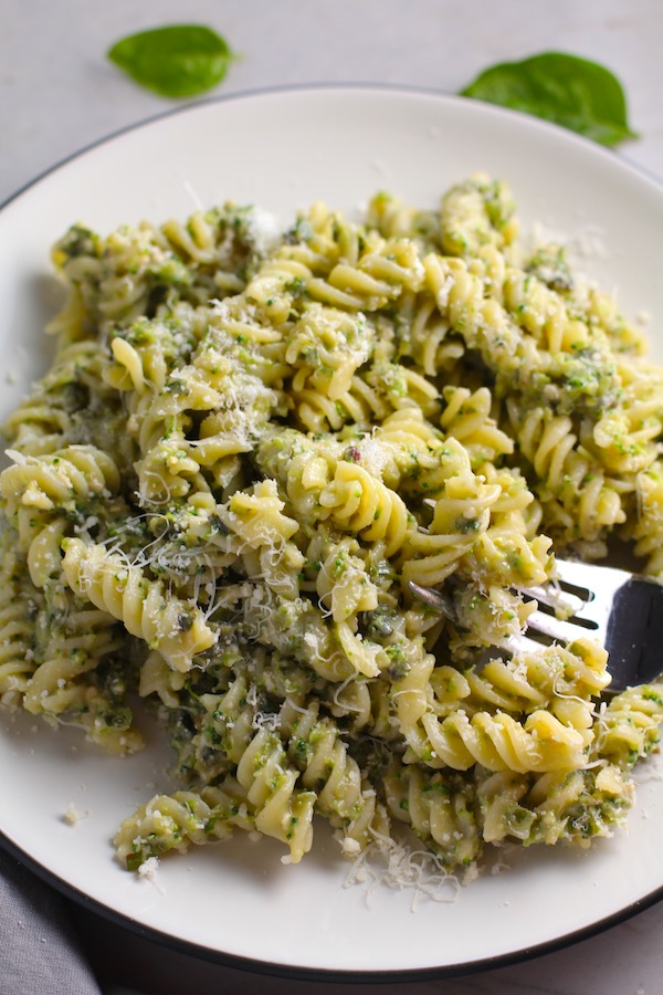 Broccoli Pesto Pasta on a plate with fork in pasta. It's delicious AND good for you! It has all of the classic pesto flavors from garlic, basil, parmesan cheese, and pine nuts. But the flavor is a bit more mellow by adding broccoli! #broccolirecipes #pesto #pasta #easydinner #dinnerideas #familydinner