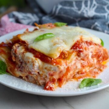 Ground Chicken Layered Lasagna Recipe on a plate with fresh basil with casserole dish in background. from the dish. This Italian Sausage-style chicken Lasagne Recipe is the stuff that dreams are made of. Layers of pasta, creamy ricotta, salty chewy mozzarella, salty and hearty Italian Sausage, and sweet and tangy tomato sauce.