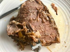 Fork scraping off fat layer from cooked brisket for Smoky Pulled Beef Brisket. It's smokey, savory, tender, moist, and full of flavor. In a delicious sauce, it goes great on a sandwich, over polenta, on rice, or potatoes. #slowcooker #crockpot #brisket #beefbrisket #pulledbeef #pulledpork