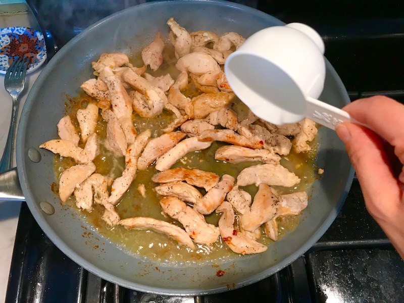 Measuring cup pouring water over cooked chicken in pan for Chicken Mushroom Stroganoff with spinach. It has a thick, creamy, savory mushroom sauce with a touch of tangy sour cream. #chickendinners #chickenrecipes #familydinners #dinnerideas