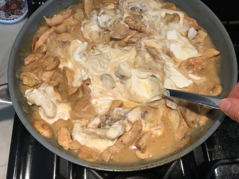 Mixing sour cream into chicken and mushroom sauce in skillet for Chicken Mushroom Stroganoff with spinach. It has a thick, creamy, savory mushroom sauce with a touch of tangy sour cream. #chickendinners #chickenrecipes #familydinners #dinnerideas