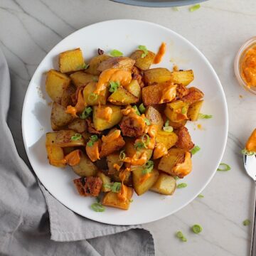 Patatas Bravas with chorizo on a plate with chorizo and creamy Paprika aioli drizzled over top. This Patatas Bravas Recipe, or Spicy Potatoes, is easy, indulgent, and utterly delicious!