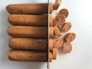 Sliced sausage on cutting board with knife for Mediterranean SHEET PAN DINNER with chicken sausage, parmesan zucchini. and crispy chickpeas. Serve over quinoa with dollops of seasoned Ricotta. #sheetpandinner #chickpeas