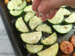 Hand sprinkling parmesan on zucchini for Mediterranean SHEET PAN DINNER with chicken sausage, parmesan zucchini. and crispy chickpeas. Serve over quinoa with dollops of seasoned Ricotta. #sheetpandinner #chickpeas