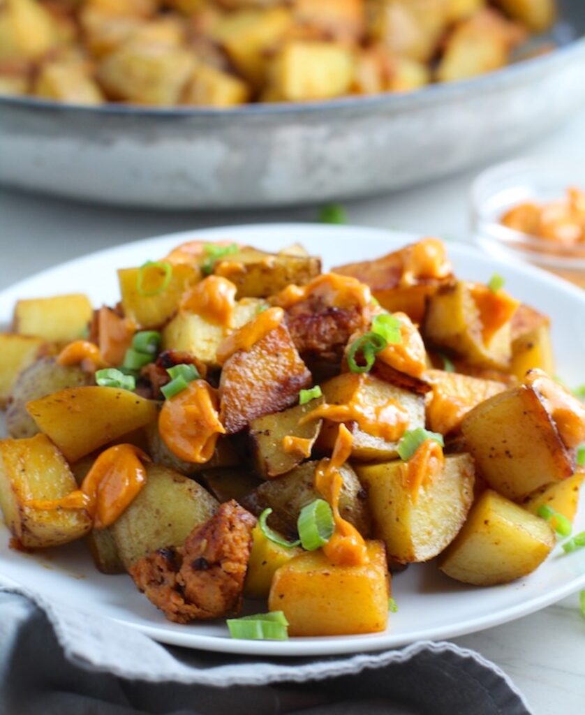Patatas Bravas with chorizo on a plate with chorizo and creamy Paprika aioli drizzled over top. This Patatas Bravas Recipe, or Spicy Potatoes, is easy, indulgent, and utterly delicious!