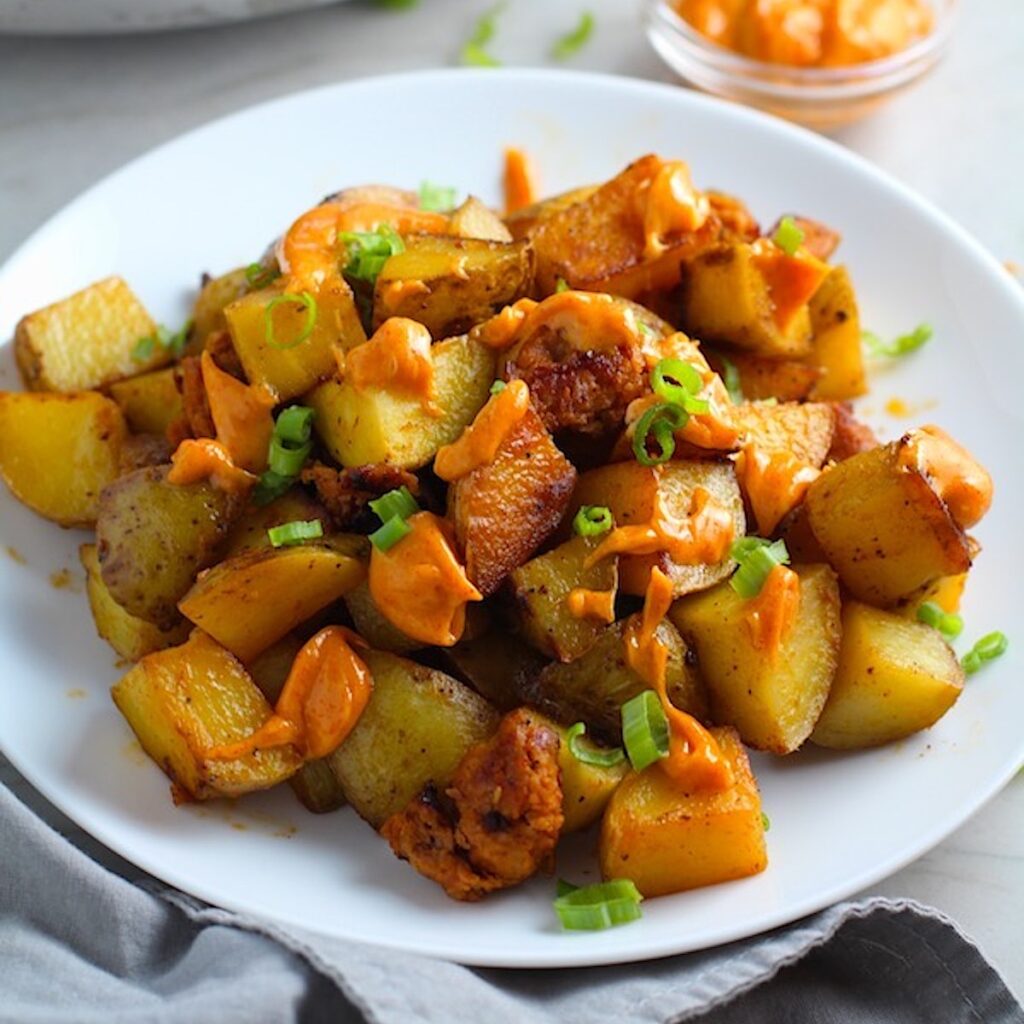 Patatas Bravas with chorizo on a plate with chorizo and creamy Paprika aioli drizzled over top. This Patatas Bravas Recipe, or Spicy Potatoes, is easy, indulgent, and utterly delicious!
