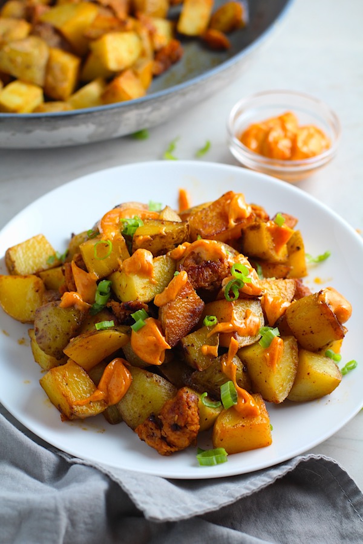 Patatas Bravas with chorizo on a plate with chorizo and creamy Paprika aioli drizzled over top. This Patatas Bravas Recipe, or Spicy Potatoes, is easy, indulgent, and utterly delicious!