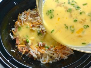 Pouring raw eggs over hash browns, cheese, chorizo in Slow Cooker for Egg Casserole with Chorizo, Potatoes and both cheddar and manchego cheeses. IT COOKS WHILE YOU SLEEP! #eggs #eggcasseroles #eggrecipes #breakfastideas #holidayrecipe