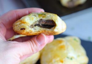 Hand holding Mini Beef Wellington Bite with bite taken. Buttery Puff Pastry is filled with a creamy mushroom and parmesan filling and tender beef filet. #appetizers #partyfood #beefrecipes #appetizerrecipes