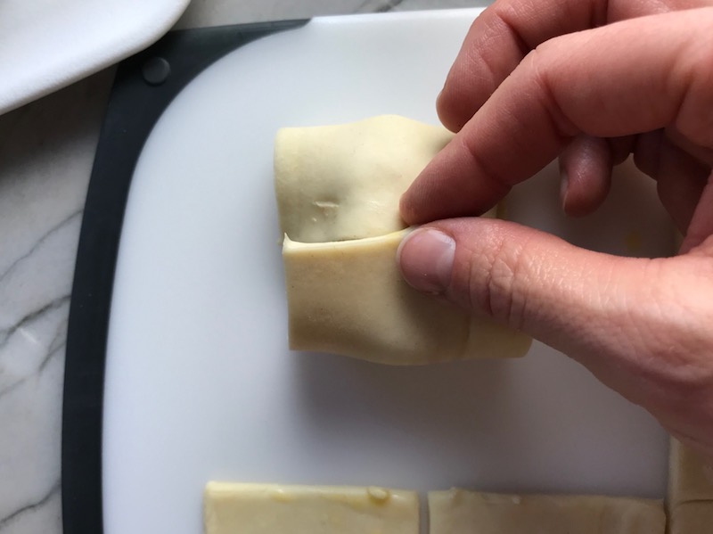 Hand folding puff pastry over filling for Mini Beef Wellington Bites. They are flaky and buttery Puff Pastry is filled with a creamy mushroom and parmesan filling and tender beef filet. #appetizers #partyfood