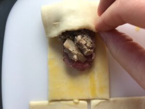 Hand folding puff pastry over filling for Mini Beef Wellington Bites. They are flaky and buttery Puff Pastry is filled with a creamy mushroom and parmesan filling and tender beef filet. #appetizers #partyfood