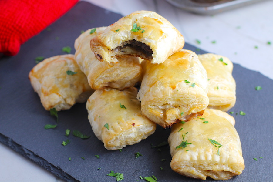 Mini Beef Wellington Bites stacked on platter. They are flaky and buttery on the outside. Puff Pastry is filled with a creamy mushroom and parmesan filling and tender beef filet. #appetizers #partyfood