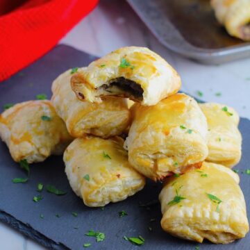 Mini Beef Wellington Bites stacked on platter. They are flaky and buttery on the outside. Puff Pastry is filled with a creamy mushroom and parmesan filling and tender beef filet.  #appetizers #partyfood
