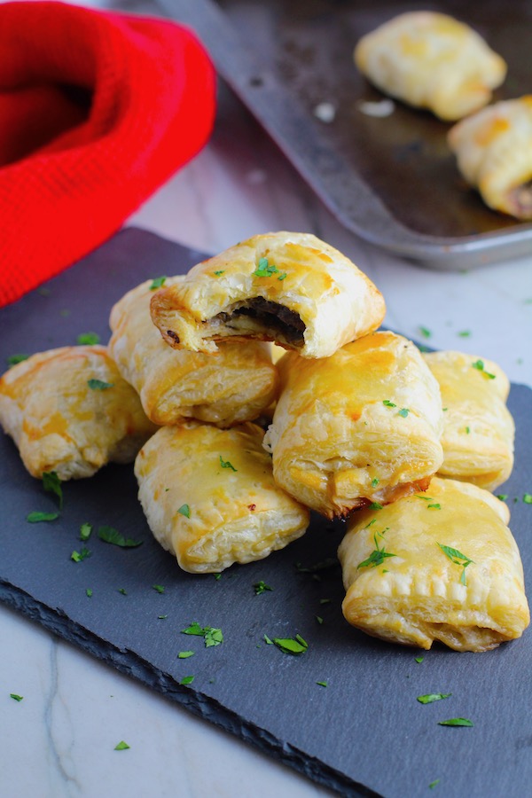 Mini Beef Wellington Bites stacked on platter. They are flaky and buttery on the outside. Puff Pastry is filled with a creamy mushroom and parmesan filling and tender beef filet. #appetizers #partyfood
