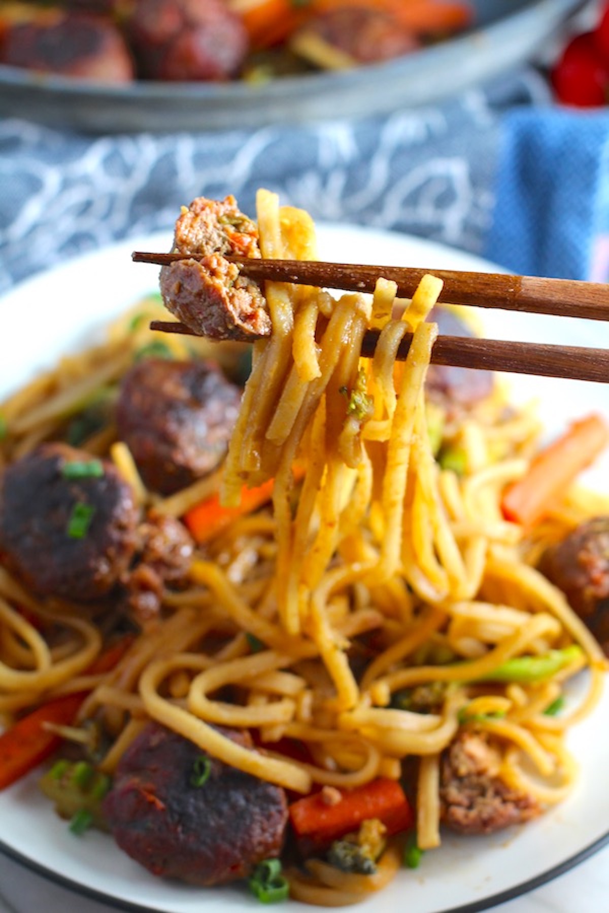 Chopsticks with bite of Teriyaki Meatball Stir Fry with Veggie Stir Fry, and rice noodles on a plate. #asianmeatballs #teriyaki #noodles #familydinner #easydinners #dinnerideas