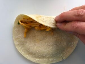 Rolling corn tortilla for Chicken Taquitos. Corn tortillas are filled with smoky taco seasoned shredded chicken, and creamy cheddar cheese. #dinnerideas #familydinner #chickenrecipes #chickendinner #tacos #taquitos