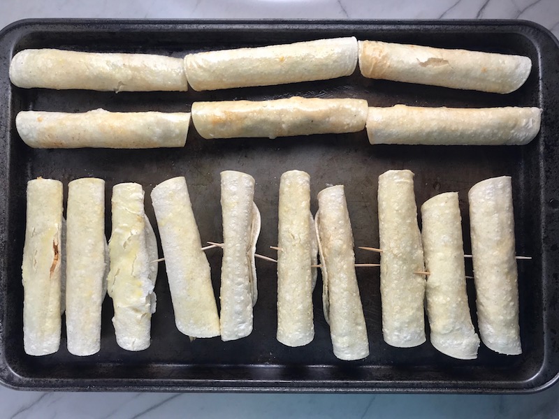 Chicken Taquitos on pan before baking. Corn tortillas are filled with smoky taco seasoned shredded chicken, and creamy cheddar cheese. #dinnerideas #familydinner #chickenrecipes #chickendinner #tacos #taquitos