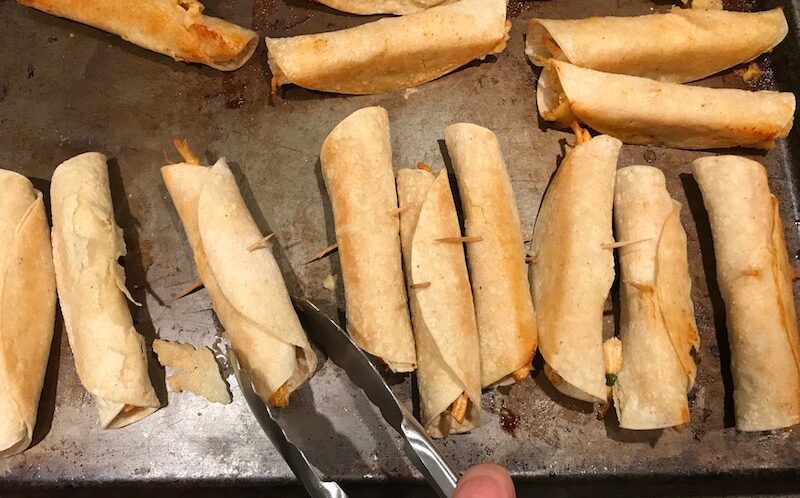 Baked Chicken Taquitos on pan. Corn tortillas are filled with smoky taco seasoned shredded chicken, and creamy cheddar cheese. #dinnerideas #familydinner #chickenrecipes #chickendinner #tacos #taquitos