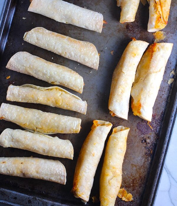 Baked Chicken Taquitos on pan. Corn tortillas are filled with smoky taco seasoned shredded chicken, and creamy cheddar cheese. #dinnerideas #familydinner #chickenrecipes #chickendinner #tacos #taquitos