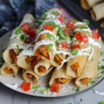 Baked Spicy Chicken Taquitos stacked on plate with toppings. Corn tortillas are filled with smoky taco seasoned shredded chicken, and creamy cheddar cheese.  #dinnerideas #familydinner #chickenrecipes #chickendinner #tacos #taquitos
