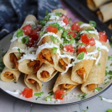 Baked Spicy Chicken Taquitos stacked on plate with toppings. Corn tortillas are filled with smoky taco seasoned shredded chicken, and creamy cheddar cheese. #dinnerideas #familydinner #chickenrecipes #chickendinner #tacos #taquitos