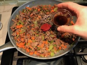 Beef filling in pan for Cottage Pie recipe. It has Spanish Chorizo and ground beef cooked in a rich and savory gravy with veggies and herbs. Creamy mashed potatoes sit on top with manchego, parmesan, and garlic. #dinnerideas #cottagepie #shepherdspie