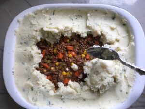 Covering filling with potatoes for Cottage Pie recipe. It has Spanish Chorizo and ground beef cooked in a rich and savory gravy with veggies and herbs. Creamy mashed potatoes sit on top with manchego, parmesan, and garlic. #dinnerideas #cottagepie #shepherdspie