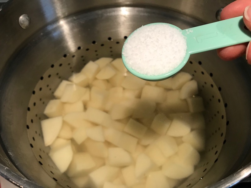 Adding salt to water with potatoes for Cottage Pie recipe. It has Spanish Chorizo and ground beef cooked in a rich and savory gravy with veggies and herbs. Creamy mashed potatoes sit on top with manchego, parmesan, and garlic. #dinnerideas #cottagepie #shepherdspie