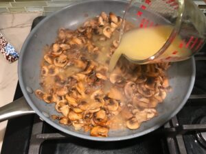 Adding broth to cooked sliced Mushrooms in skillet for this Heavenly Mushroom Sauce Recipe. #vegetarian #healthydinner #dinnerideas #mushrooms