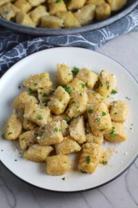 Gnocchi on plate with parmesan and parsley. Cauliflower Gnocchi are soft, silky, buttery, and melt-in-your-mouth! Made with cauliflower, they're a healthier version to traditional gnocchi! Add my simple Garlic Butter Sauce or Tomato Sauce and they are heaven. #dinnerideas #gnocchi #cauliflower