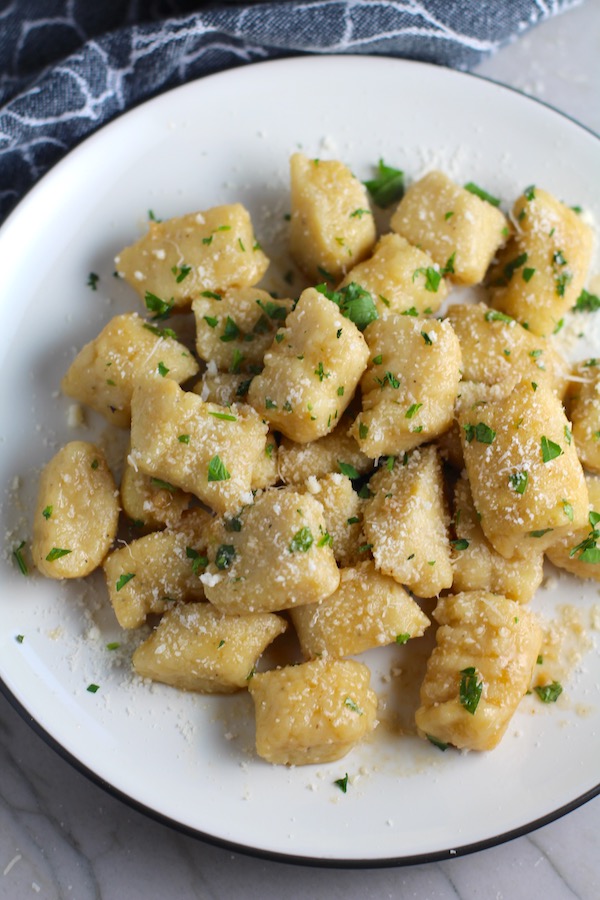 Gnocchi on plate with parmesan and parsley. Cauliflower Gnocchi are soft, silky, buttery, and melt-in-your-mouth! Made with cauliflower, they're a healthier version to traditional gnocchi! Add my simple Garlic Butter Sauce or Tomato Sauce and they are heaven. #dinnerideas #gnocchi #cauliflower