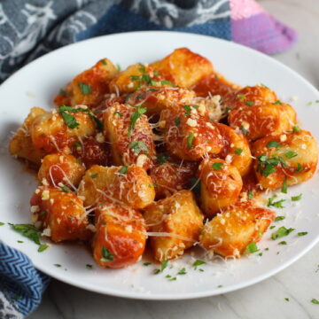 Cauliflower Gnocchi in tomato sauce on plate with parmesan and parsley. They are soft, silky, buttery, and melt-in-your-mouth! Made with cauliflower, they're a healthier version to traditional gnocchi! Add my simple Garlic Butter Sauce or Tomato Sauce and they are heaven. #dinnerideas #gnocchi #cauliflower