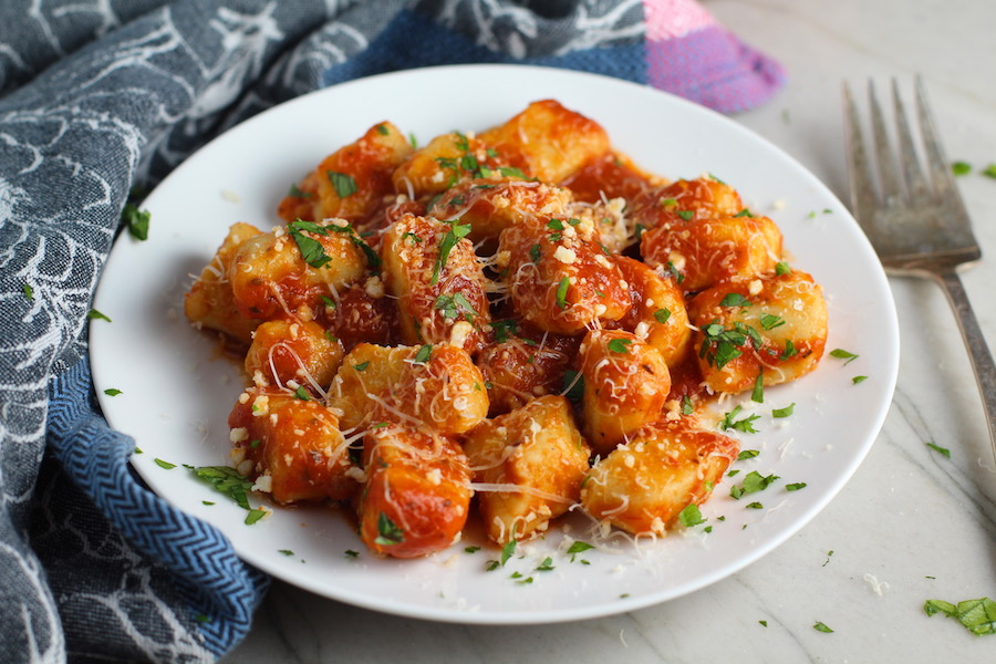 Cauliflower Gnocchi in tomato sauce on plate with parmesan and parsley. They are soft, silky, buttery, and melt-in-your-mouth! Made with cauliflower, they're a healthier version to traditional gnocchi! Add my simple Garlic Butter Sauce or Tomato Sauce and they are heaven. #dinnerideas #gnocchi #cauliflower