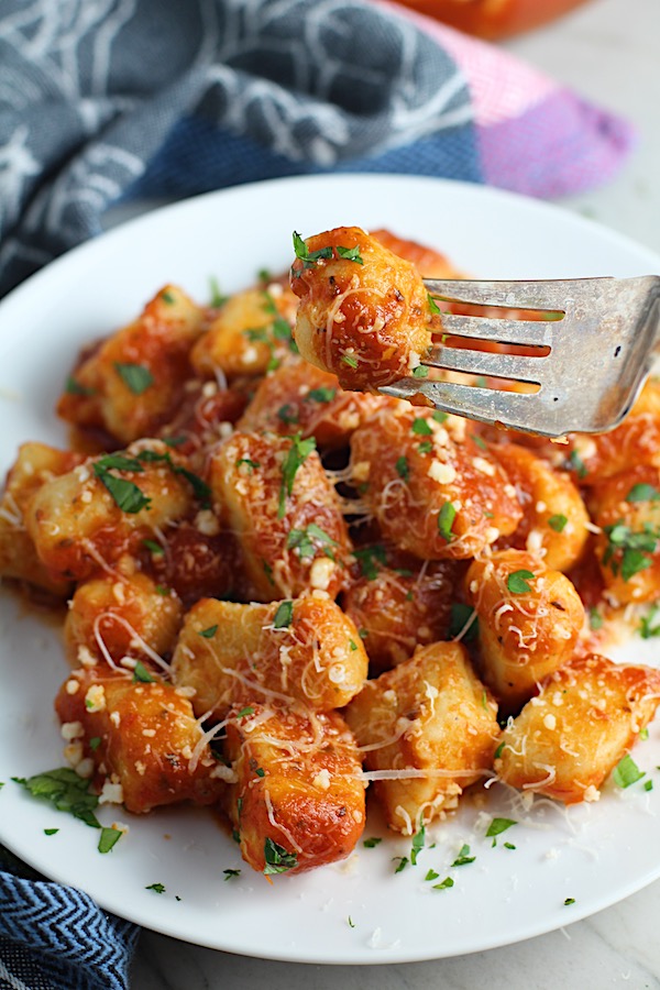 Cauliflower Gnocchi in tomato sauce on fork and on plate with parmesan and parsley. They are soft, silky, buttery, and melt-in-your-mouth! Made with cauliflower, they're a healthier version to traditional gnocchi! Add my simple Garlic Butter Sauce or Tomato Sauce and they are heaven. #dinnerideas #gnocchi #cauliflower