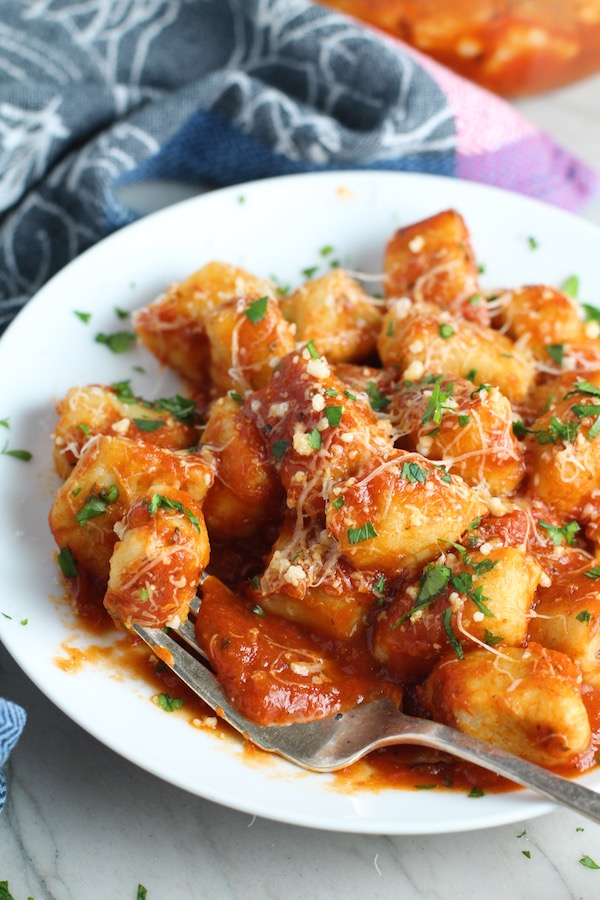 Cauliflower Gnocchi in tomato sauce on plate with parmesan and parsley. They are soft, silky, buttery, and melt-in-your-mouth! Made with cauliflower, they're a healthier version to traditional gnocchi! Add my simple Garlic Butter Sauce or Tomato Sauce and they are heaven. #dinnerideas #gnocchi #cauliflower