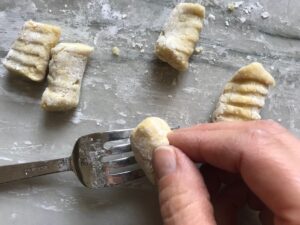 Rolling gnocchi on fork on for cauliflower gnocchi. These Gnocchi are soft, silky, buttery, and melt-in-your-mouth! Made with cauliflower, they're a healthier version to traditional gnocchi! Add my simple Garlic Butter Sauce or Tomato Sauce and they are heaven.  #dinnerideas #gnocchi #cauliflower