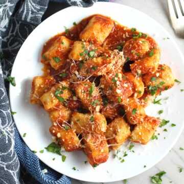 Cauliflower Gluten Free Gnocchi recipe in tomato sauce on plate with parmesan and parsley. They are soft, silky, buttery, and melt-in-your-mouth! Made with cauliflower, they're a healthier version to traditional gnocchi! Add my simple Garlic Butter Sauce or Tomato Sauce and they are heaven.