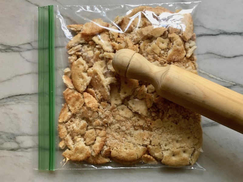Crushing crackers in bag for Bacon Mac and Cheese. It has a creamy and cheesy sauce with a touch of smokiness from the bacon, coats each piece of pasta. On top, crispy crunchy, indulgent bacon fat cracker crumbs!