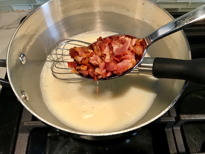 Adding cooked bacon bits to sauce for Bacon Mac and Cheese. It has a creamy and cheesy sauce with a touch of smokiness from the bacon, coats each piece of pasta. On top, crispy crunchy, indulgent bacon fat cracker crumbs!